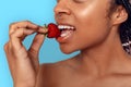 Beauty Concept. Young african woman isolated on blue biting strawberry smiling joyful mouth close-up Royalty Free Stock Photo
