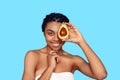 Beauty Concept. Young african woman isolated on blue covering eye with avocado posing smiling cheerful