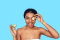 Beauty Concept. Young african woman isolated on blue covering eye with cucumber smiling playful