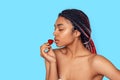 Beauty Concept. Young african woman isolated on blue foretasting strawberry delightful Royalty Free Stock Photo