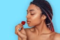 Beauty Concept. Young african woman isolated on blue looking at strawberry curious close-up Royalty Free Stock Photo