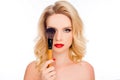 Beauty and cosmetology concept. Close up portrait of pretty blond with bright makeup hiding eye behind make-up brush isolated on