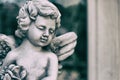 Beauty Cupid statue of Angel in vintage garden on summer. Holding bouquet flowers in his hand Royalty Free Stock Photo