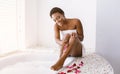 Beauty day. Smiling african american girl removes hair with razor, sitting near bath