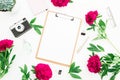 Beauty decorated concept. Blogger or freelancer workspace desk with clipboard, notebook, retro camera, peonies and pen on white ba