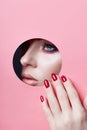 Beauty face red makeup plump lips red nails of a young girl in a round slit hole of pink paper. Woman with beautiful makeup plump