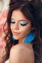 Beauty fashion model girl with creative art makeup and blue feather earring. Portrait of Beautiful brunette posing in studio, Royalty Free Stock Photo