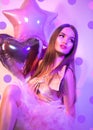 Beauty fashion model party Valentine`s Day girl with heart shaped air balloons, sitting on chair, laughing in neon light Royalty Free Stock Photo