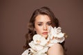 Beauty fashion portrait of perfect young stylish female model woman with curly hair holds white flowers on dark brown background Royalty Free Stock Photo