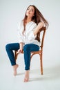 Beauty fashion portrait of smiling sensual asian young woman with dark long hair in white shirt sitting on chair on white Royalty Free Stock Photo