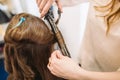 Beauty, hairstyle concept, happy young woman and hairdresser with hair iron making hairdo at hair salon. Woman Having Royalty Free Stock Photo