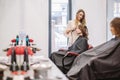 Beauty, hairstyle concept, happy young woman and hairdresser with hair iron making hairdo at hair salon. Woman Having Royalty Free Stock Photo