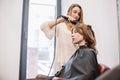 Beauty, hairstyle concept, happy young woman and hairdresser with hair iron making hairdo at hair salon. Woman Having Royalty Free Stock Photo