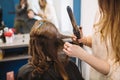 Beauty, hairstyle concept, happy young woman and hairdresser with hair iron making hairdo at hair salon. Woman Having Royalty Free Stock Photo