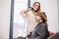 Beauty, hairstyle concept, happy young woman and hairdresser with hair iron making hairdo at hair salon. Woman Having Royalty Free Stock Photo