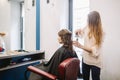 Beauty, hairstyle concept, happy young woman and hairdresser with hair iron making hairdo at hair salon. Woman Having