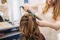 Beauty, hairstyle concept, happy young woman and hairdresser with hair iron making hairdo at hair salon. Woman Having Royalty Free Stock Photo