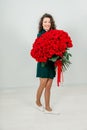Portrait of a satisfied young woman dressed in green dress holding huge bouquet of roses  over white background. Royalty Free Stock Photo