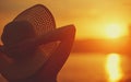 Beauty happy woman in her hat is back and admire sunset over sea Royalty Free Stock Photo