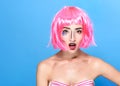 Beauty head shot. Surprised Young woman with creative pop art make up and pink wig looking at the camera on blue background