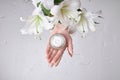 Beauty jar cream hand cosmetic woman with lily flowers lie on table, jar cream product in hand woman on wet flower mirror Royalty Free Stock Photo