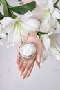 Beauty jar cream hand cosmetic woman with lily flowers lie on table, jar cream product in hand woman on wet flower mirror Royalty Free Stock Photo