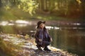 Beauty kid girl with long hair sitting near the river at the sunny evening