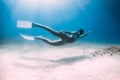 Beauty lady freediver underwater glides with white fins. Attractive woman freediver in blue ocean with sun rays