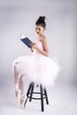 Beauty lady is wearing pink ballet dress and pink satin ballet shoes,sitting on black chair and read book Royalty Free Stock Photo