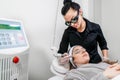 Beauty laser technician performing a cosmetic skin resurfacing session on a female patient, also called a laser peel or photofacia