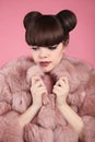Beauty makeup. Fashion teen girl model in pink fur coat. Brunette with matte lips and bun hairstyle posing over studio background.
