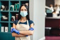 Beauty master in protective mask and gloves standing at hairdresser`s interior, empty space