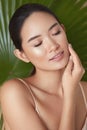 Beauty. Model Face On Palm Background. Asian Woman With Closed Eyes Enjoying Smooth, Hydrated And Glowing Skin.