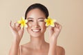 Beauty. Model With Flowers Portrait. Happy Asian Girl With Tropical Plumeria Near Face Against Beige Background.