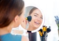 Beauty model girl applying makeup and smiling. Beautiful young woman looking in the mirror and applying cosmetics Royalty Free Stock Photo