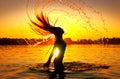 Beauty model girl splashing water with her hair. Girl silhouette over sunset sky. Swimming and splashing on summer beach