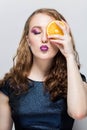 Beauty Model Girl takes Juicy Oranges. Professional make up. Orange Slice holds hand and closes one eye, pouts her lips, eyes clos Royalty Free Stock Photo