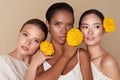 Beauty. Models With Flowers Portrait. Group Of Diversity Women Holding Yellow Marigolds And Posing Against Beige Background.
