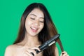 Beauty natural healthy Asian woman using hair straightener over green isolated background Royalty Free Stock Photo