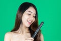 Beauty natural healthy Asian woman using hair straightener over green isolated background Royalty Free Stock Photo