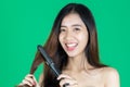 Beauty natural healthy Asian woman using hair straightener over green isolated background Royalty Free Stock Photo