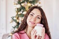 Beauty, people, holidays, skin care and cosmetics concept - young woman with a can of moisturizer in hand on christmas tree lights