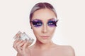 Woman with artistic purple blue eyes makeup feather on eyelashes holding showing perfume silver jewelry on head