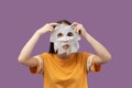 Beauty and personal care. Girl puts on a fabric mask to rejuvenate and moisturize her face, isolated on pink background