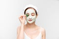 Beauty portrait of Asain woman in towel on head with white nourishing mask on face and green leaf in hand, white background