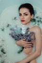 Beauty portrait of a beautiful naked young girl in a bath with milk and flowers of lilac Royalty Free Stock Photo