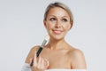 Beauty portrait of blonde smiling woman 35 year plus holding blush brush near clean fresh face  on white background Royalty Free Stock Photo