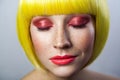 Beauty portrait of calm cute young female model with freckles, red makeup and yellow wig, closed eyes with relaxed serious face