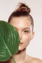 Beauty portrait of charm young girl with green plant leaf over white studio background. Cosmetics, natural