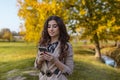 Beauty portrait of a cheerful girl with curly brunette hair in elegant suit reading on cell phone, in the park.